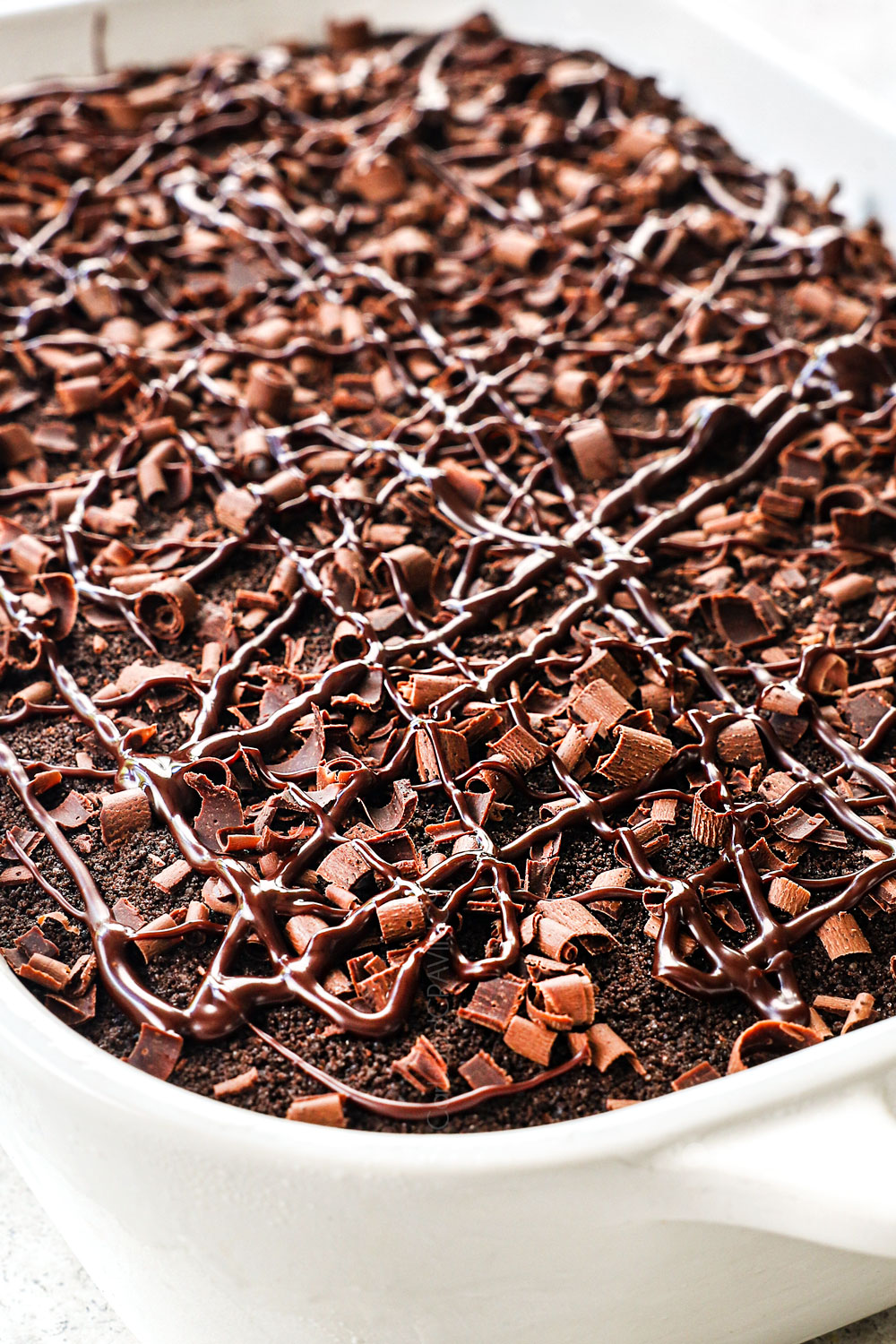 showing how to make chocolate lasagna recipe by covering the whipped topping layer with crushed Oreos, chocolate ganache drizzle and chocolate shavings