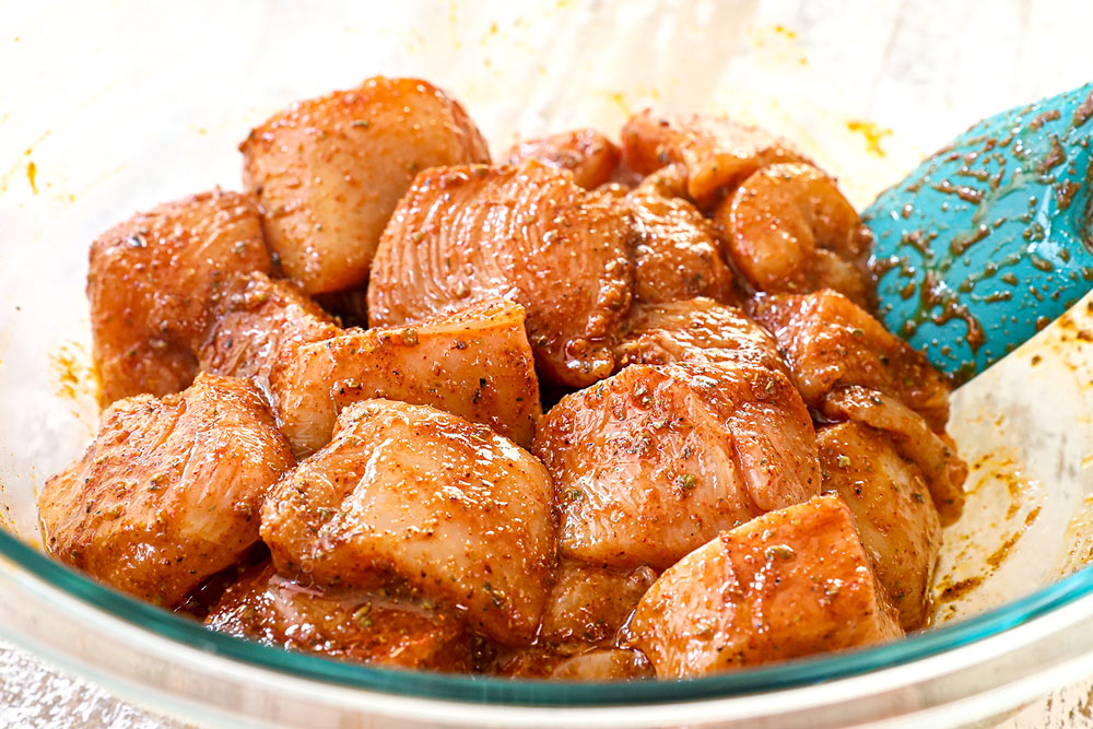 showing how to make Greek Chicken Kabobs by marinating cubed chicken in chicken kabob marinade in a bowl
