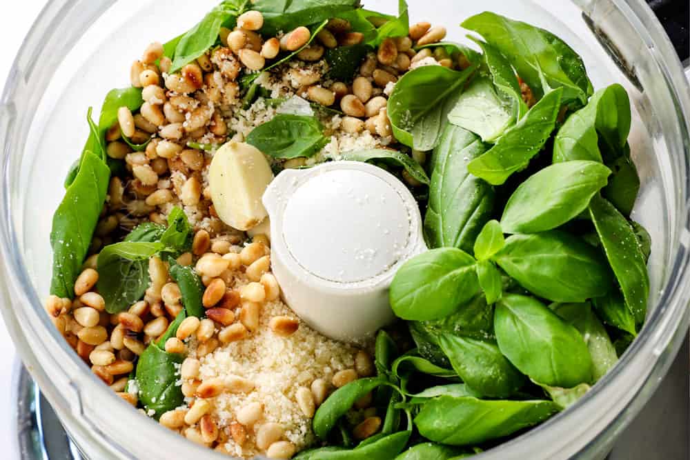 showing how to make pesto by adding basil, pine nuts, Parmesan, garlic to a food processor