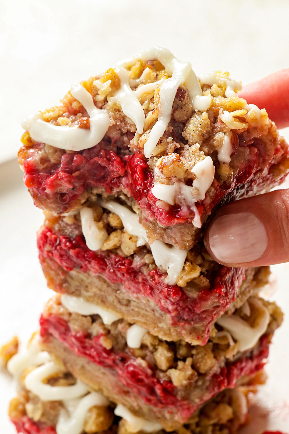 up close of raspberry bars with a bite taken out showing the raspberry filling made with real raspberries