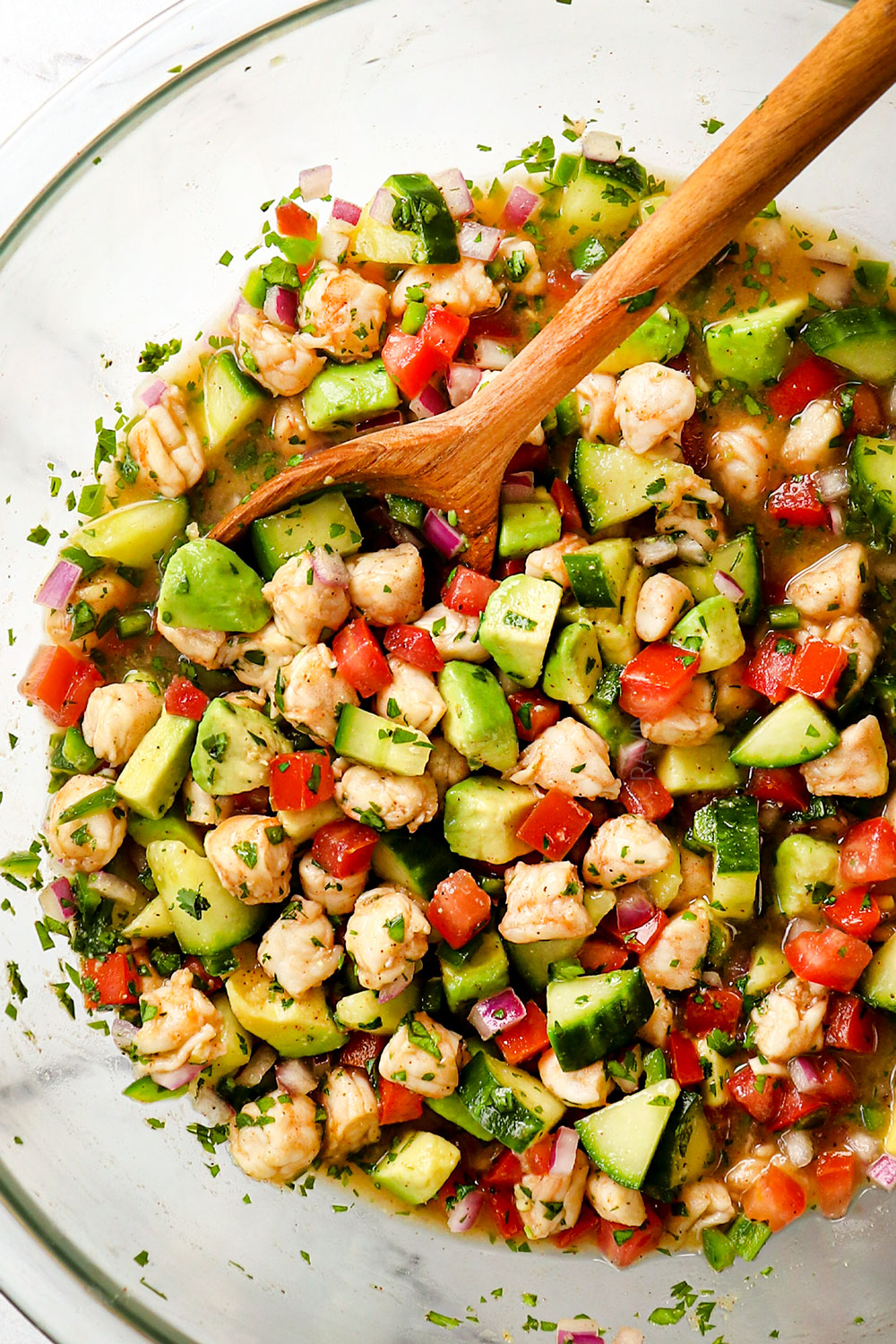 showing how to make shrimp ceviche recipe (ceviche de camaron) by stirring in chopped avocados and clamato juice