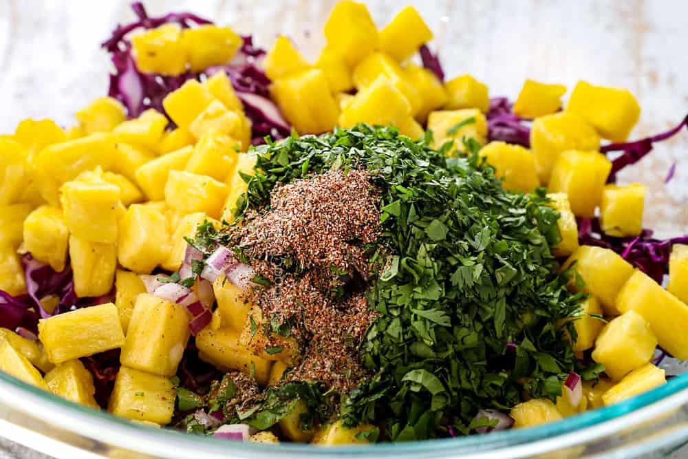 showing how to make jerk chicken tacos by adding all of the pineapple slaw ingredients to a bowl