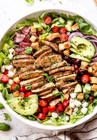 top view showing how to make Mediterranean Chicken Salad by assembling the chicken salad recipe with chicken, tomatoes, cucumbers, olives, red onions and avocado