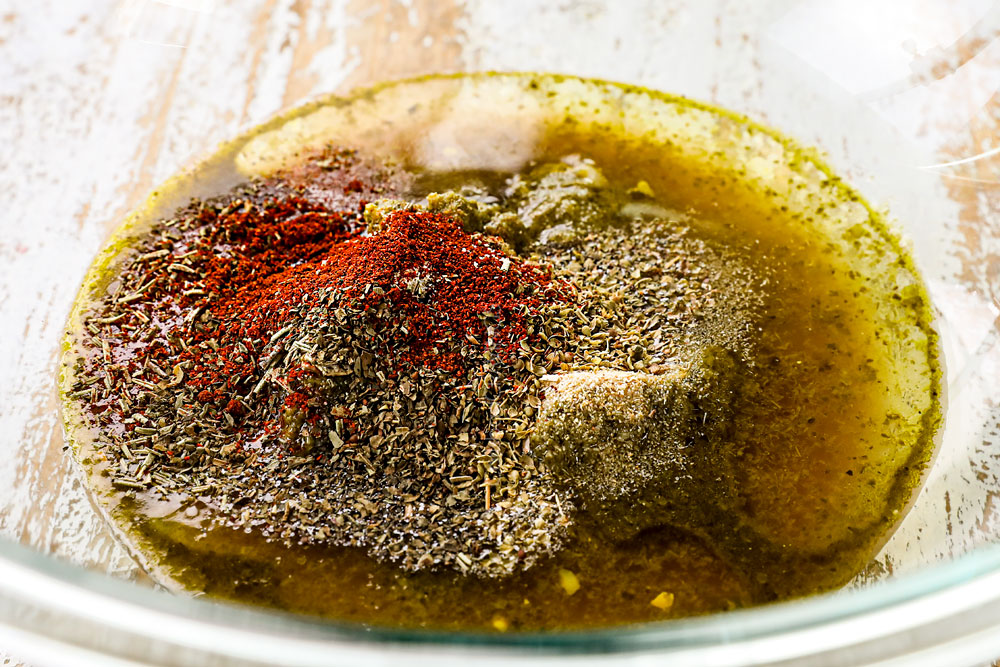 showing how to make Mediterranean Chicken Salad recipe by whisking the marinade ingredients together in a bowl that doubles as the dressing