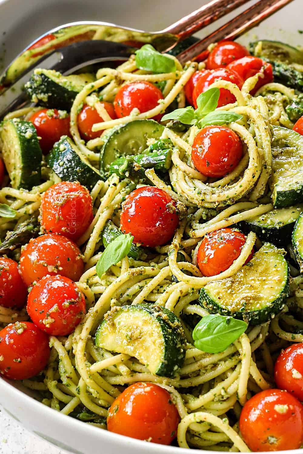 showing how to make pesto pasta recipe by tossing pesto, pasta and roasted vegetables in a large bowl