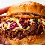 showing how to make BBQ pulled pork sandwiches by topping buns with pulled pork, with coleslaw and fried onion rings