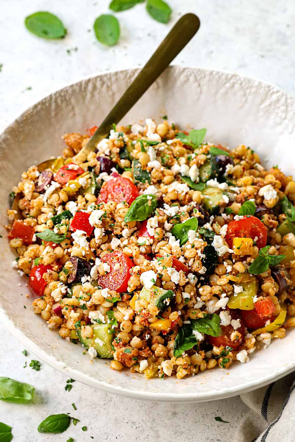 adding couscous salad recipe to a bowl with pearl couscous, tomatoes, cucumbers, feta