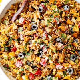 top view of taco pasta salad recipe in a white bowl with pasta, ground beef, cheese, lettuce, black beans, corn, avocados, olives, jalapenos and cilantro