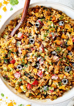 top view of taco pasta salad recipe in a white bowl with pasta, ground beef, cheese, lettuce, black beans, corn, avocados, olives, jalapenos and cilantro