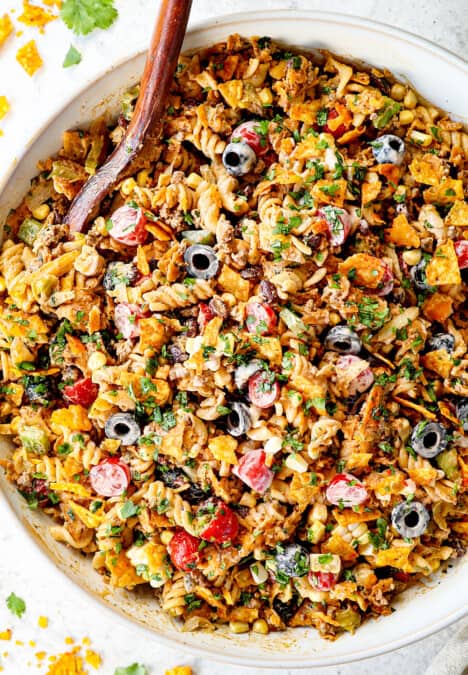 top view of taco pasta salad recipe in a white bowl with pasta, ground beef, cheese, lettuce, black beans, corn, avocados, olives, jalapenos and cilantro