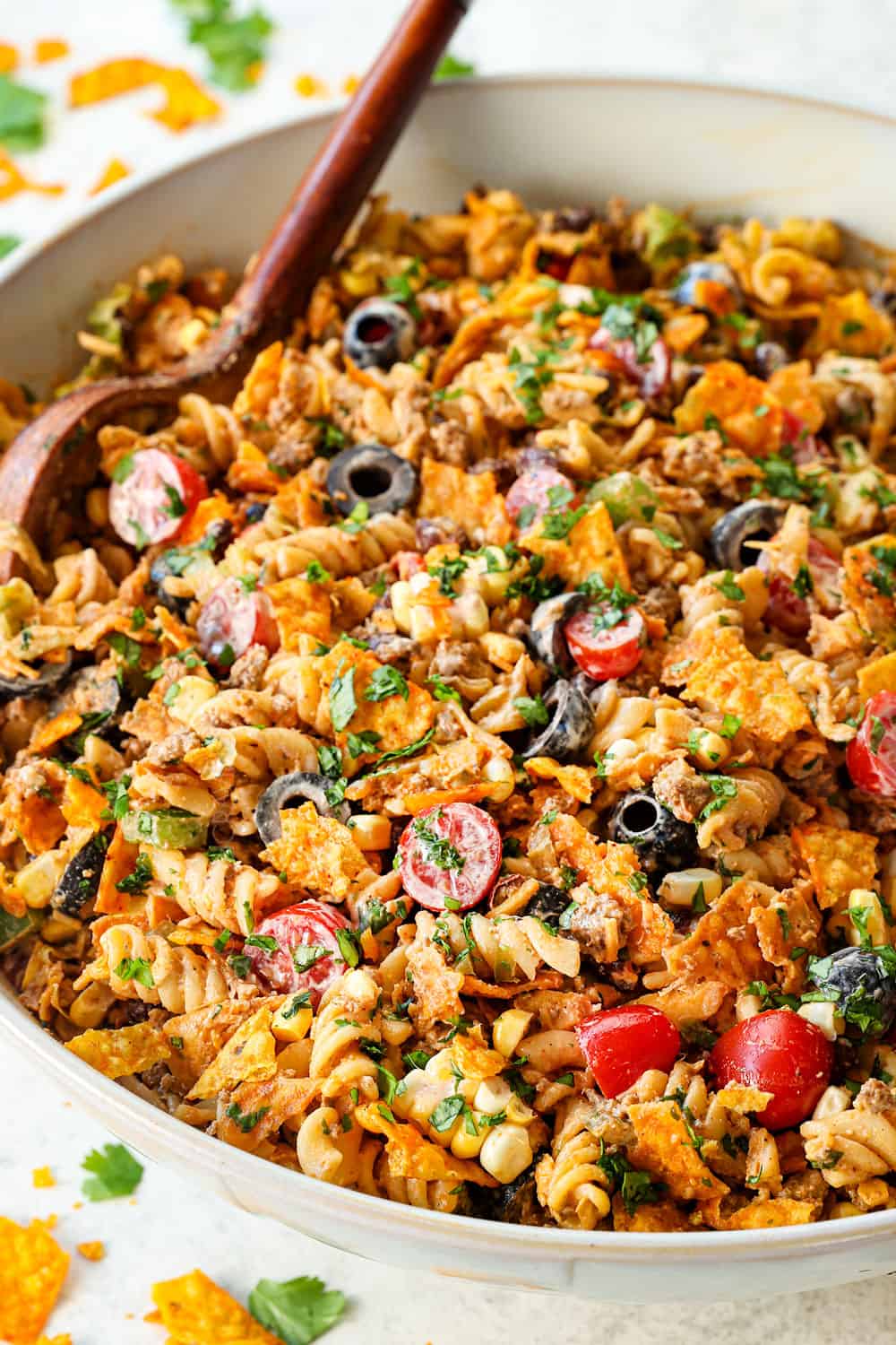 side view of taco pasta salad in a white bowl with pasta, ground beef, cheese, lettuce, black beans, avocados, etc.