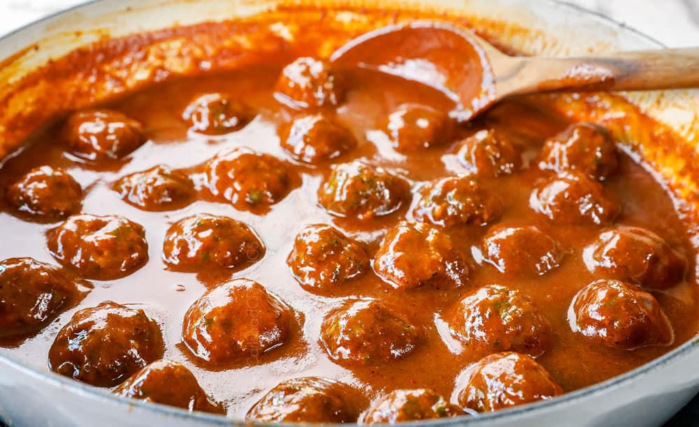 showing how to make baked enchilada meatballs by adding the meatballs to the enchilada sauce