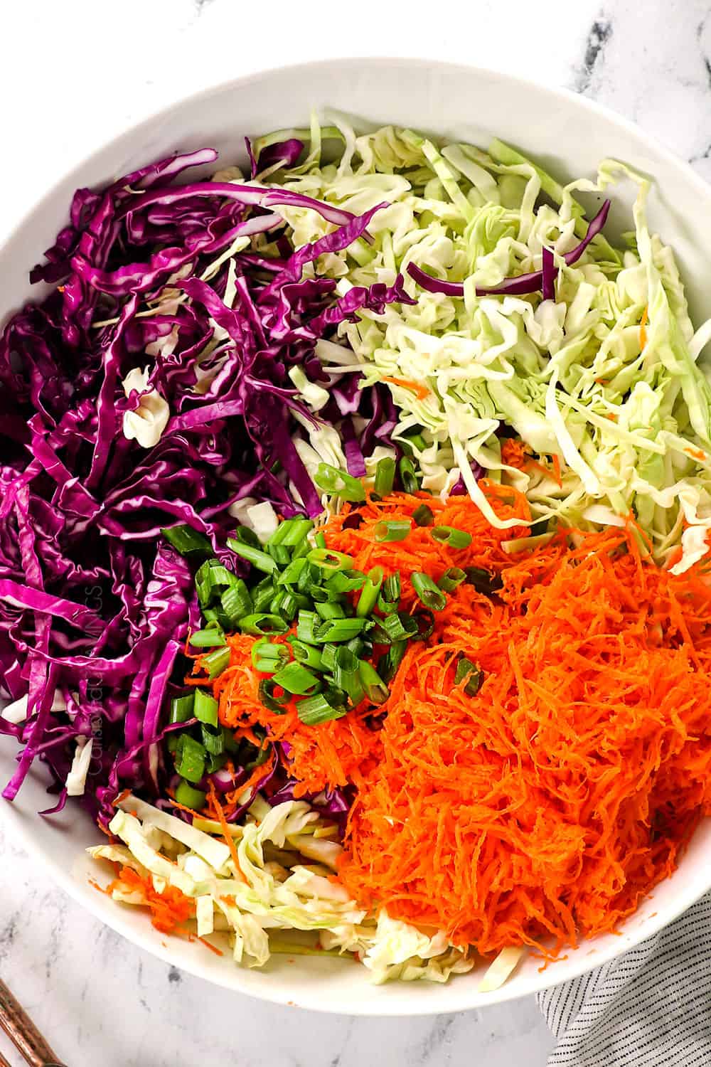 showing how to make coleslaw recipe by adding green cabbage, red cabbage, carrots and green onions to a bowl