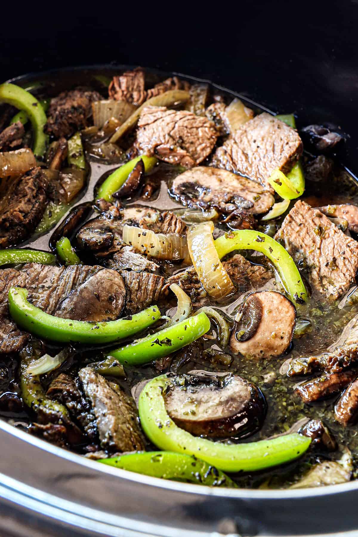showing how to make crockpot Philly cheesesteaks by cooking steak, bell peppers, onions and mushrooms in the crockpot