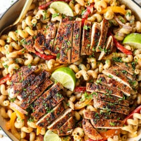 showing how to make jerk chicken pasta (Rasta pasta) by adding chicken to top of pasta with bell peppers