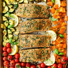 adding pesto salmon to a baking dish with tomatoes, zucchini and bell peppers
