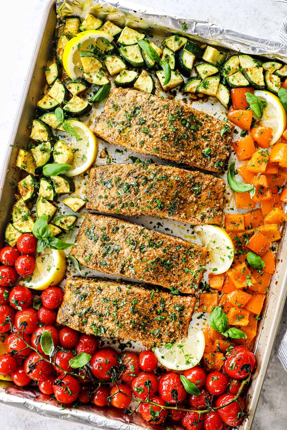 adding pesto salmon to a baking dish with tomatoes, zucchini and bell peppers