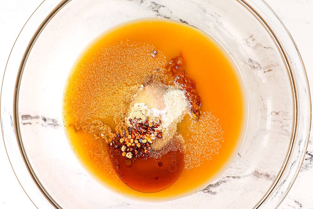 showing how to make orange beef by whisking the orange juice, orange marmalade, toasted sesame oil, hoisin, soy sauce, ginger, garlic, red pepper flakes ingredients together in a glass bowl
