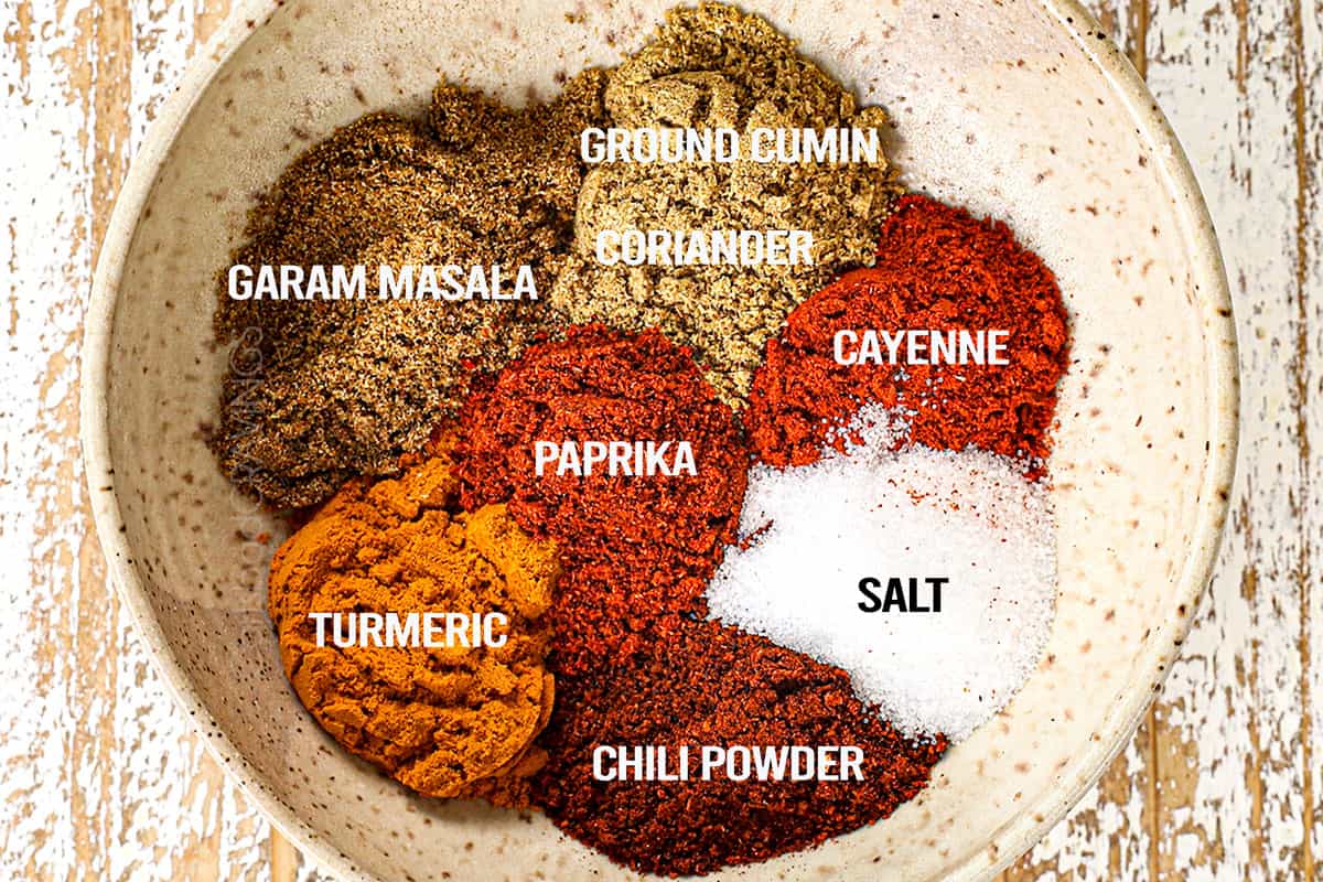 showing how to make Chicken Tikka Masala recipe by mixing together garam masala, ground cumin, coriander, paprika, cayenne, salt, chili powder and turmeric