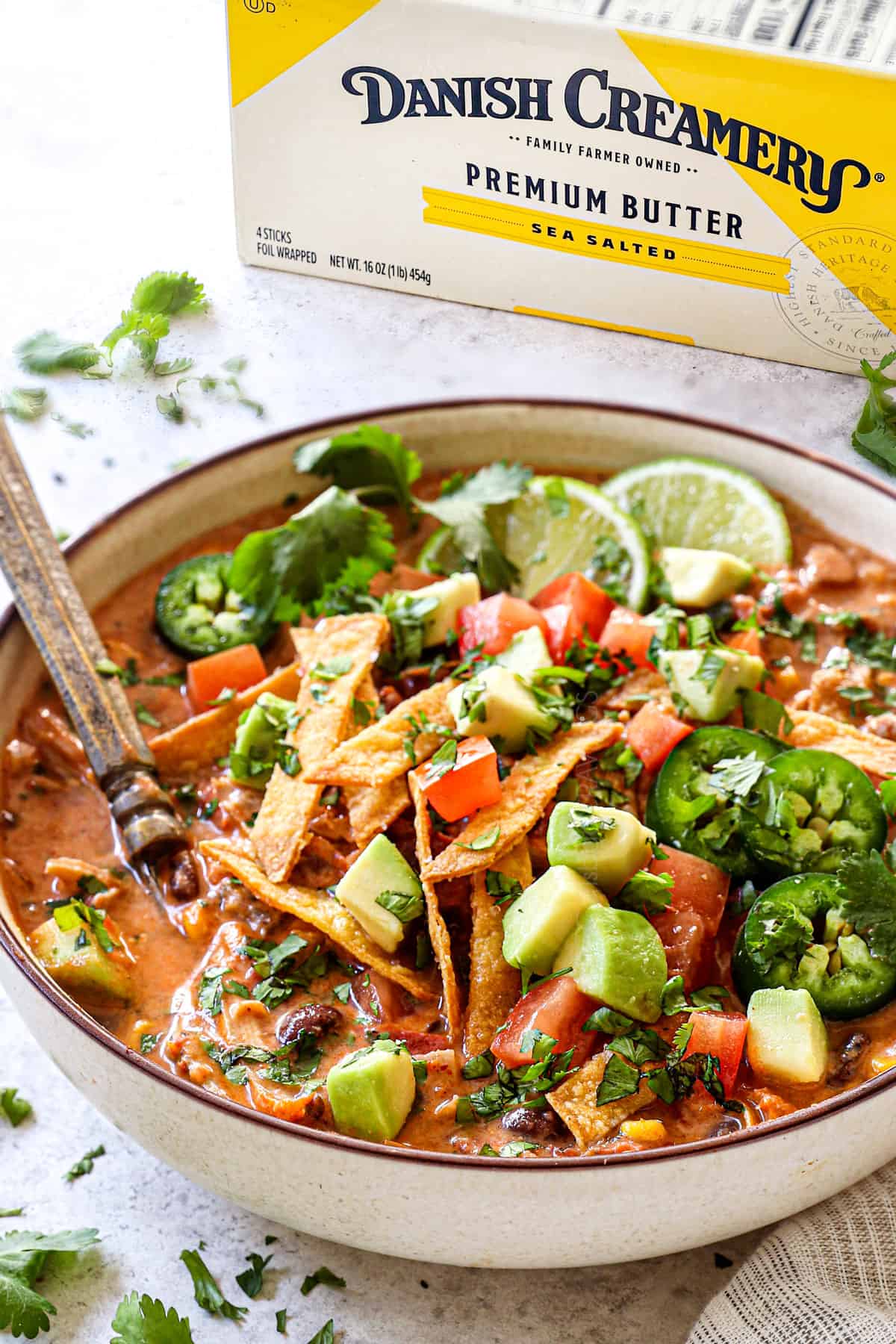 showing how to serve creamy chicken tortilla soup recipe by adding to a bowl and loading with toppings