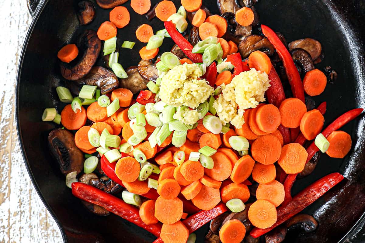 showing how to make udon noodles by stir frying carrots, bell peppers, ginger and garlic