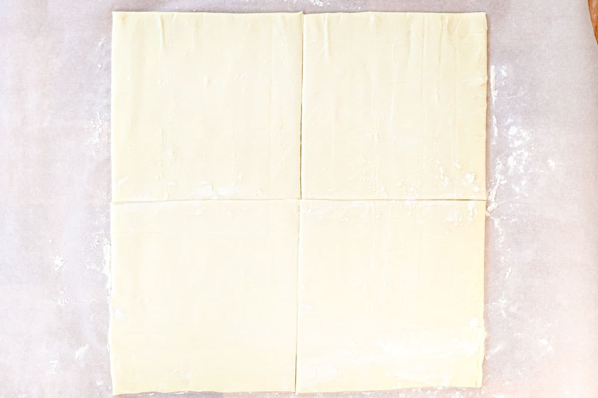 showing how to make apple turnover recipe by slicing the puff pastry into 4 equal squares using a pizza cutter