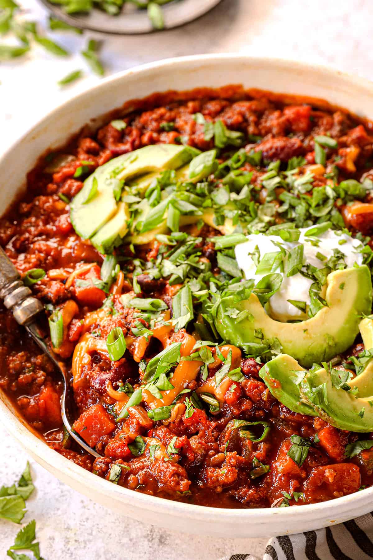 side view of pumpkin chili recipe in a bowl with turkey topped with cheese and sour cream