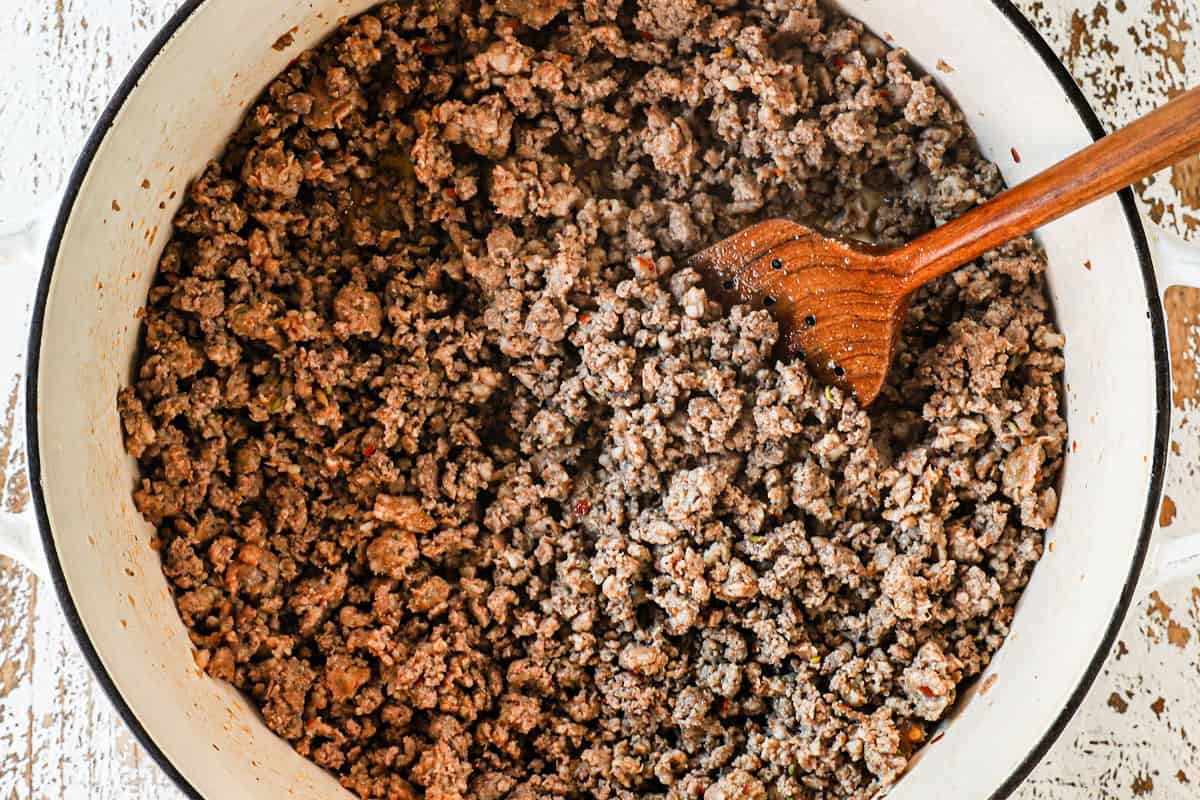 showing how to make pumpkin chili recipe by browning Italian sausage and ground beef in a Dutch oven