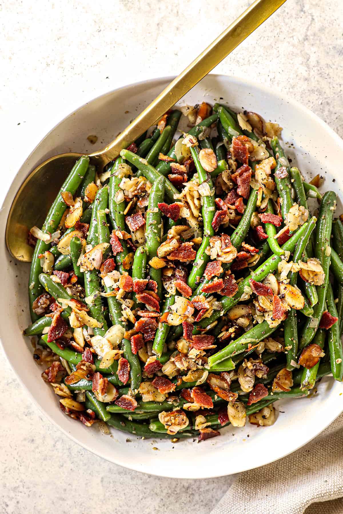 showing how to serve Green Beans Almondine by adding to a bowl and garnishing with bacon