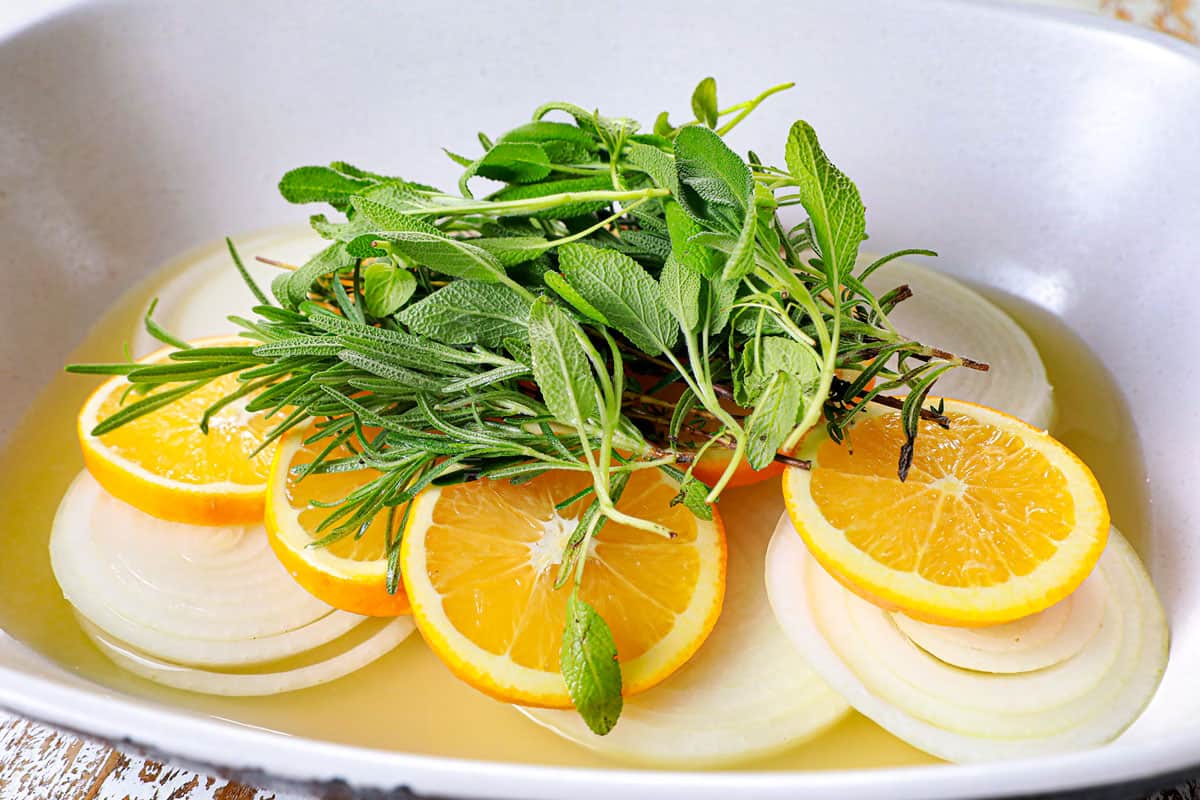showing how to make roast turkey breast recipe by lining a roasting pan with onions, carrots and fresh herbs