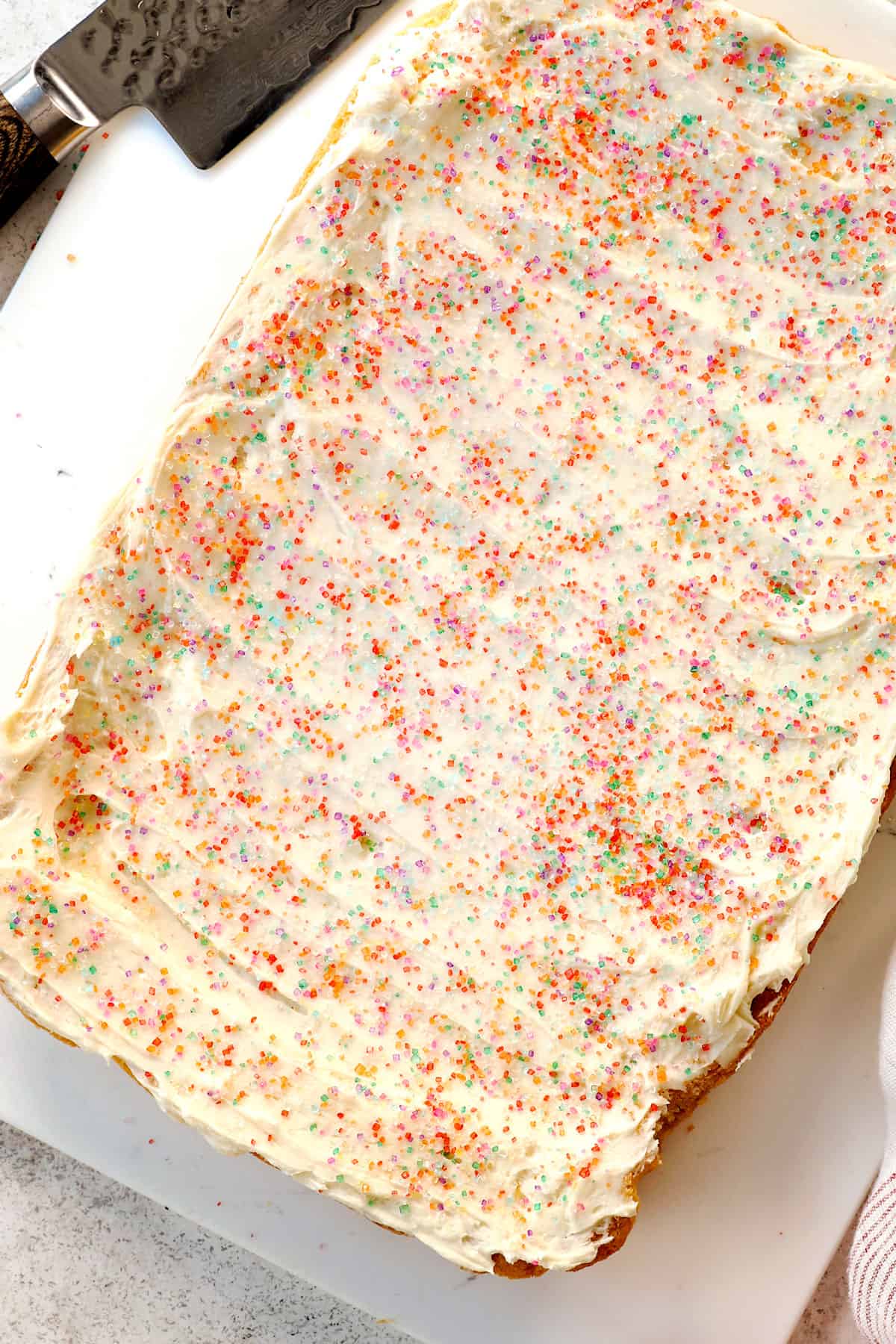 showing how to make sugar cookie bars by spreading with cream cheese frosting