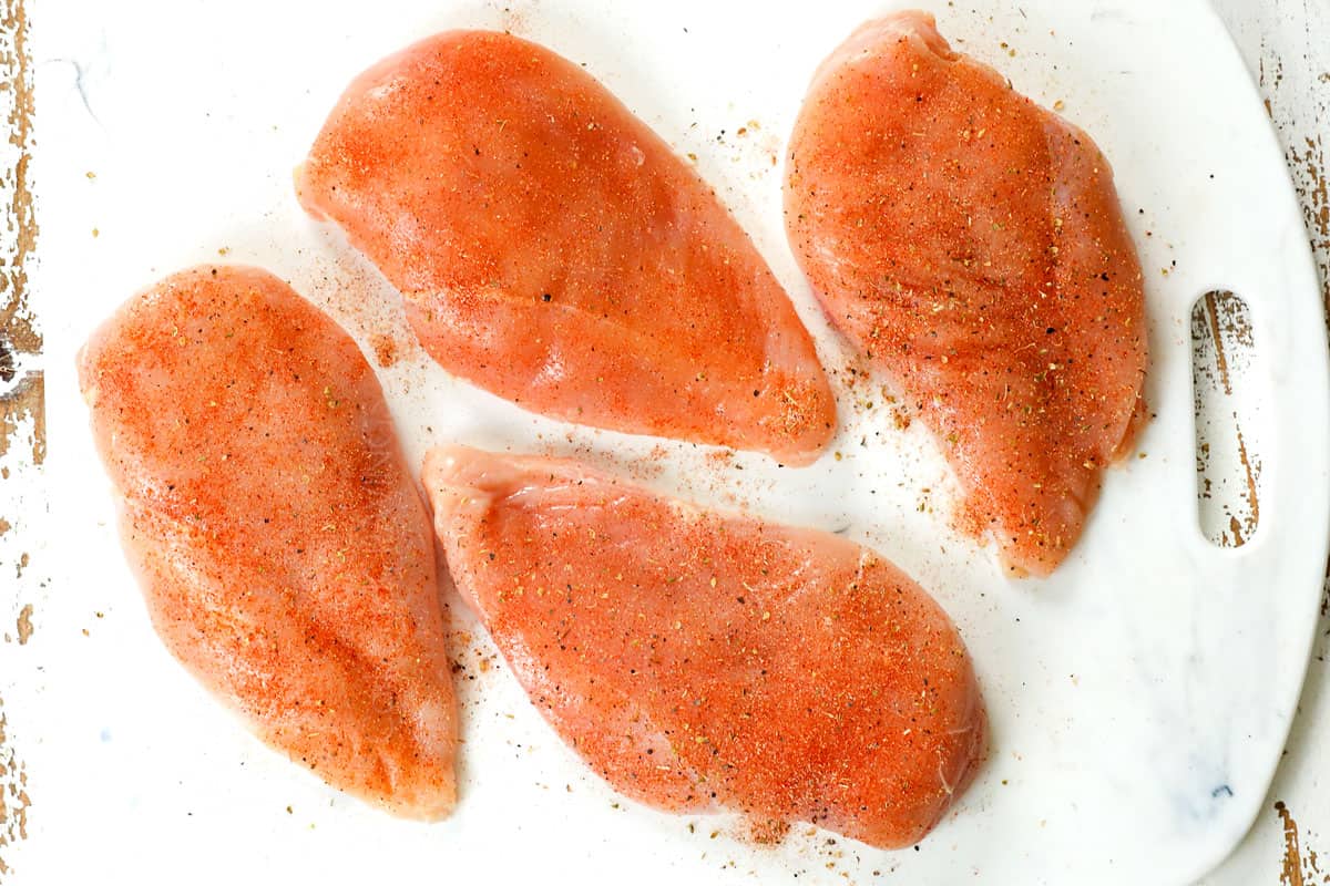 showing how to make shredded chicken by seasoning chicken breasts on a cutting board with salt, pepper, garlic powder, onion powder and paprika