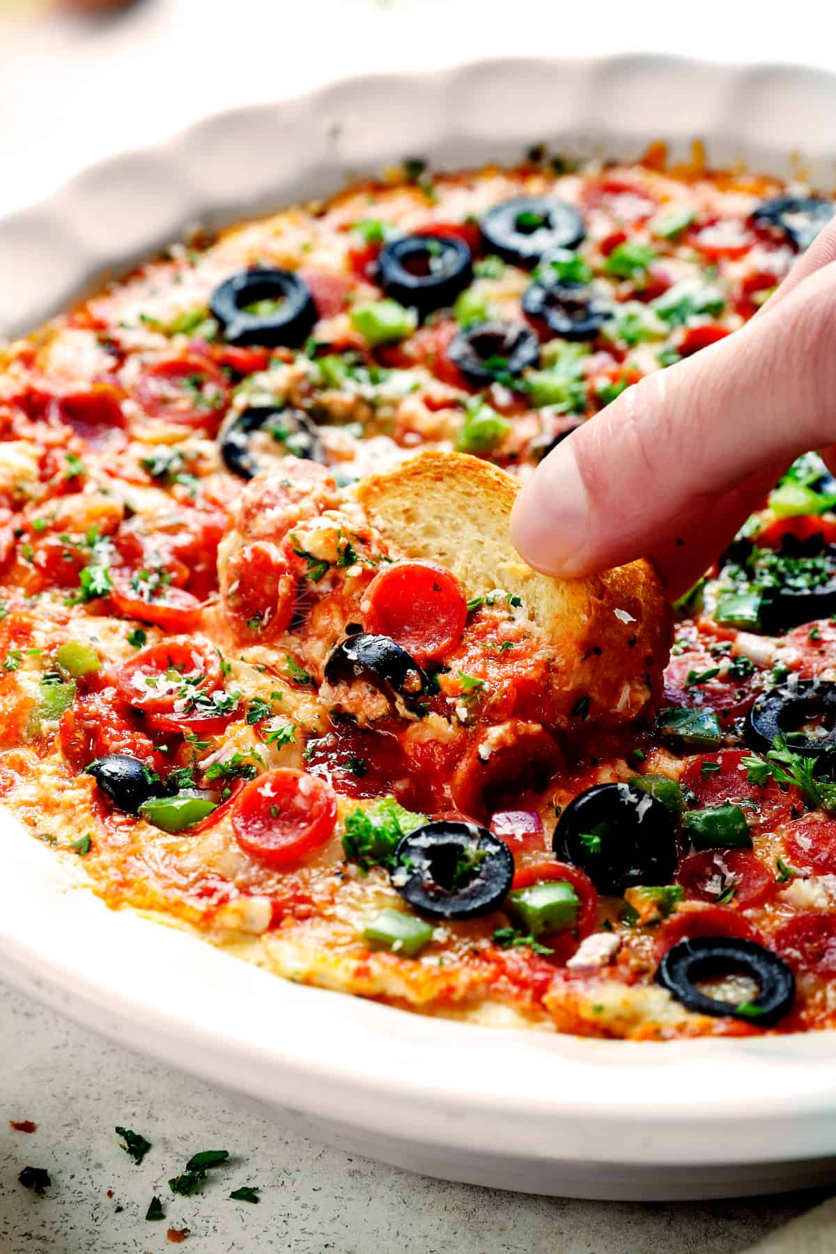 showing how to serve pizza dip by dipping baguette slices into the dip with pepperoni