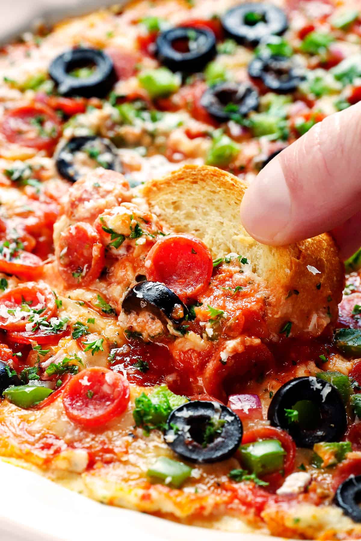 up close of scooping up baked pizza dip with a baguette slice