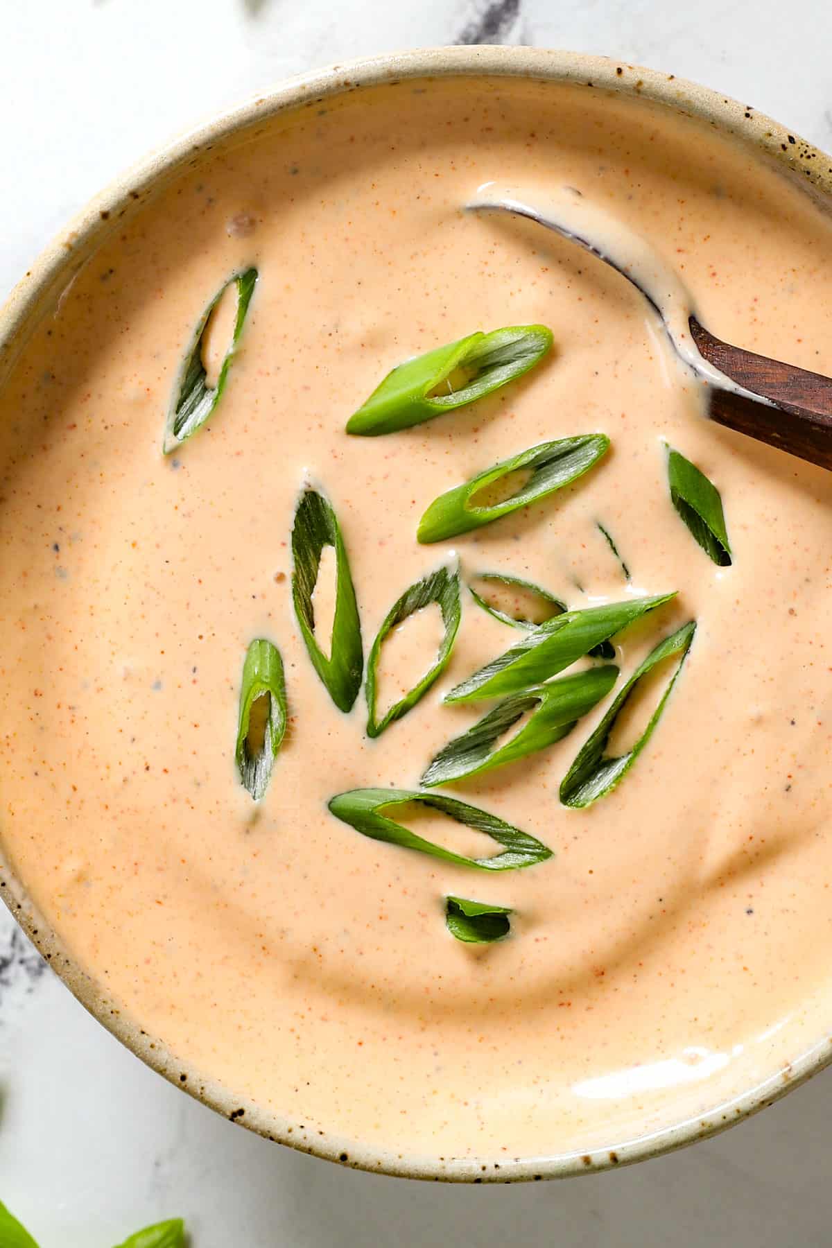 top view of homemade yum yum sauce garnished with green onions showing the pink-orange color