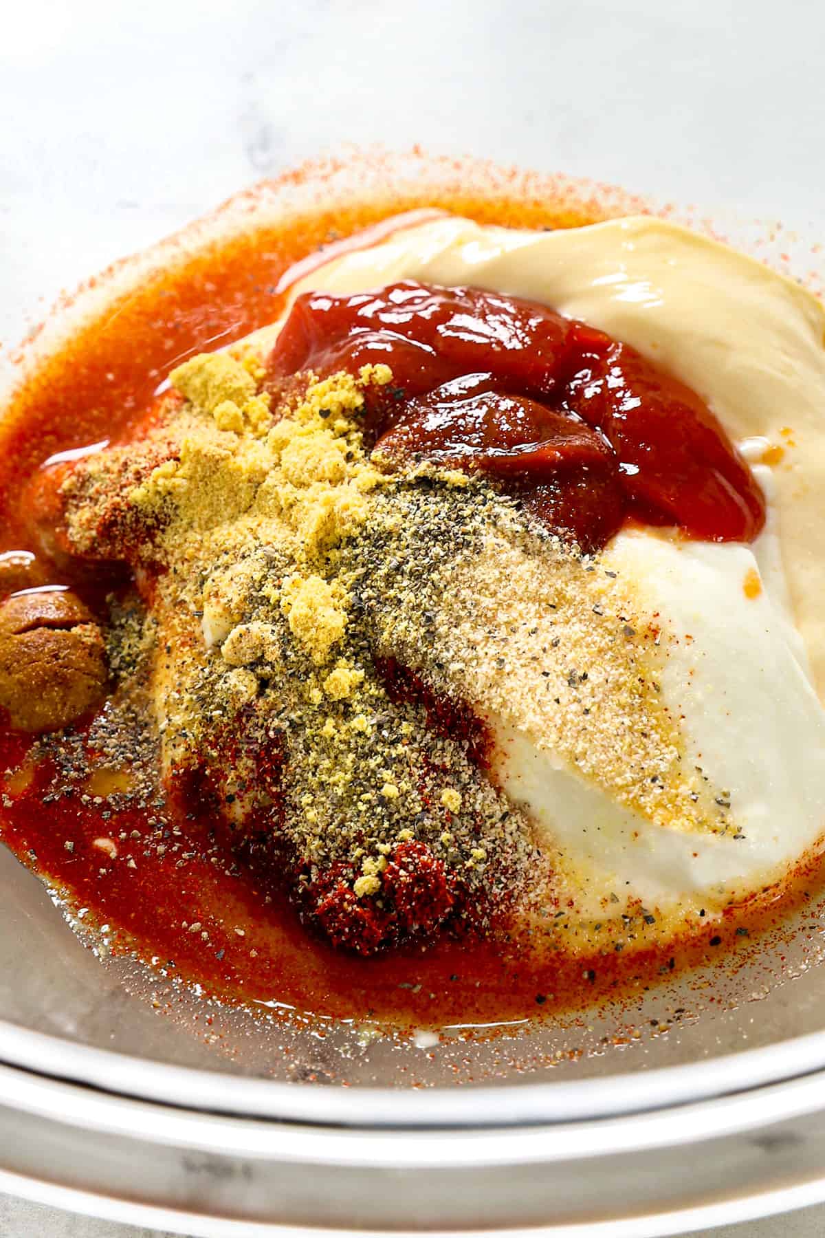 showing yum yum sauce ingredients in a mixing bowl: mayonnaise, ketchup, rice vinegar, paprika, ground mustard, ground ginger, garlic powder, salt and pepper