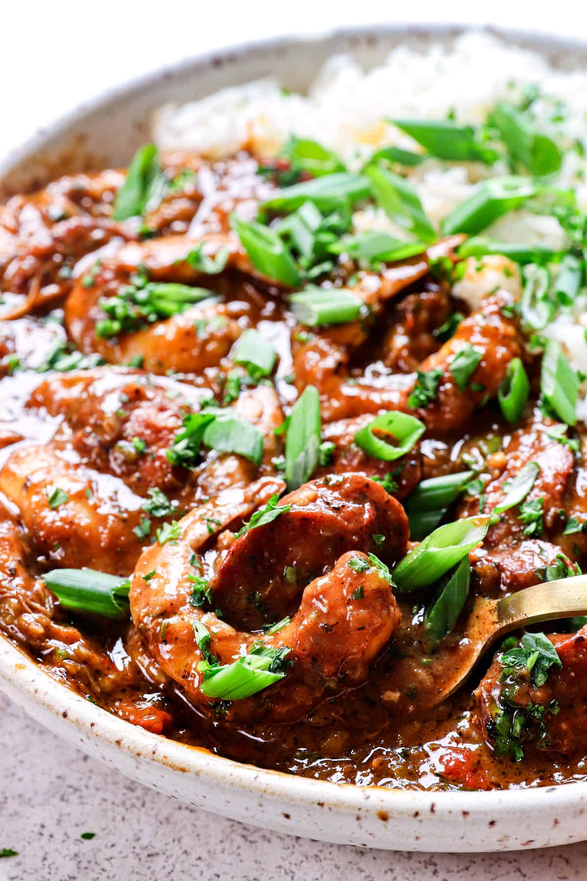 a spoon scooping up shrimp gumbo with chicken and sausage