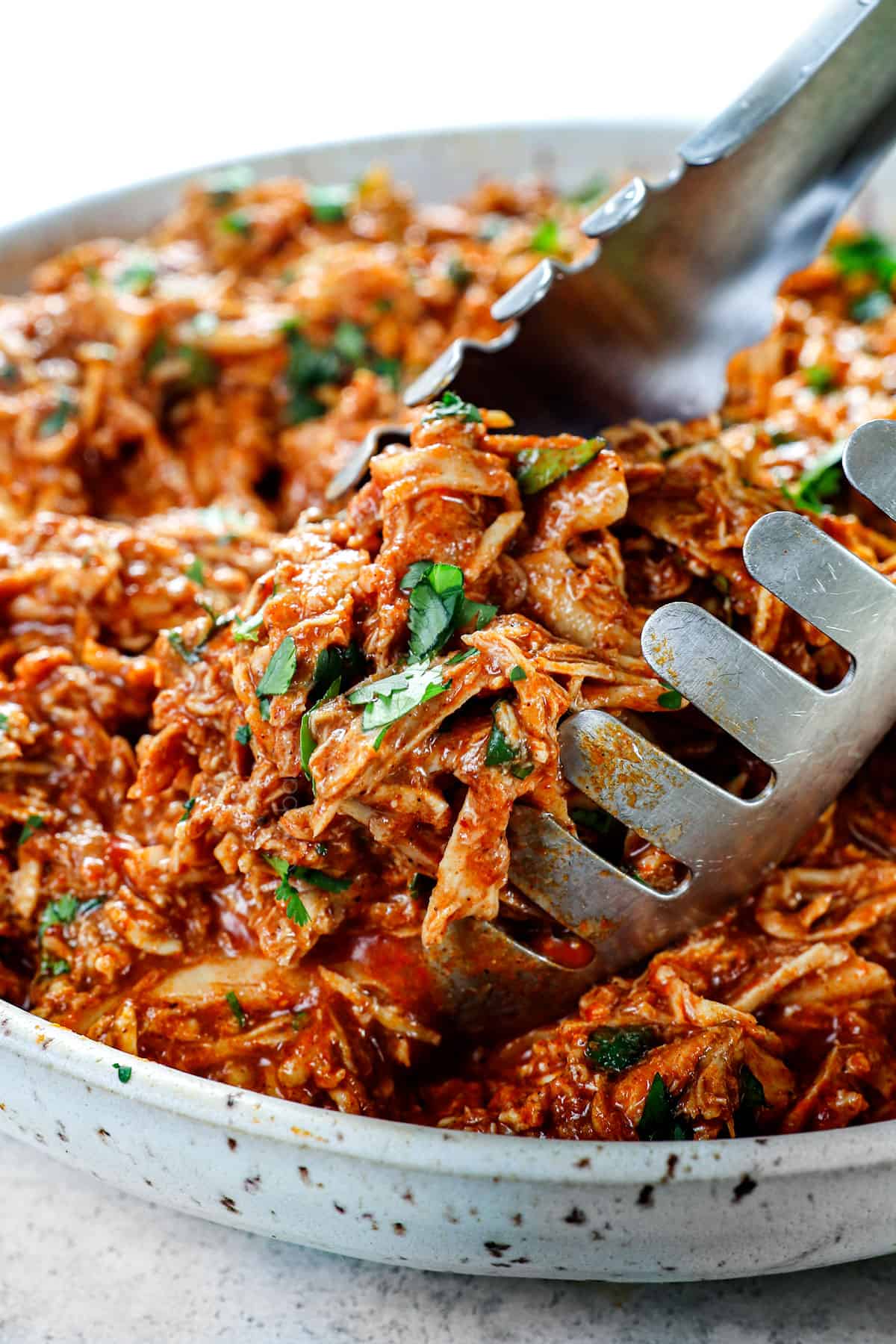 showing how to make baked chicken tacos by adding chicken to homemade enchilada sauce