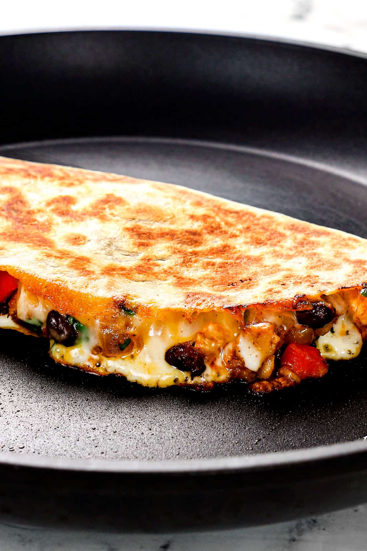 showing how to make chicken quesadillas by cooking the quesadilla in a skillet until the cheese oozes out