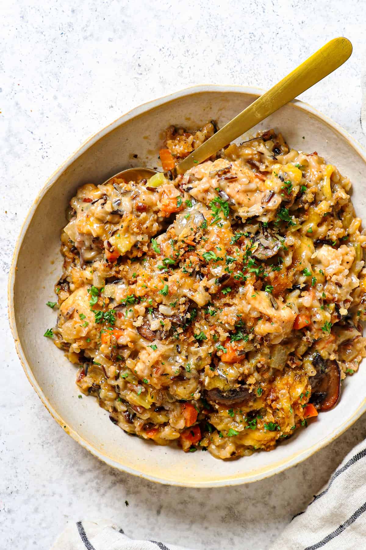 top view of chicken wild rice casserole being served in a bowl with mushrooms, carrots, celery and chicken