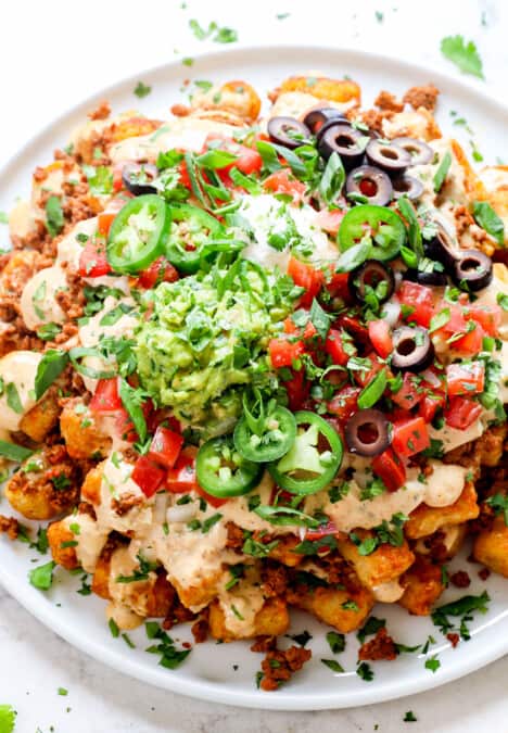 showing how to serve totchos (tater tot nachos) by adding to a platter and garnishing with cilantro, jalapenos and pico de gallo