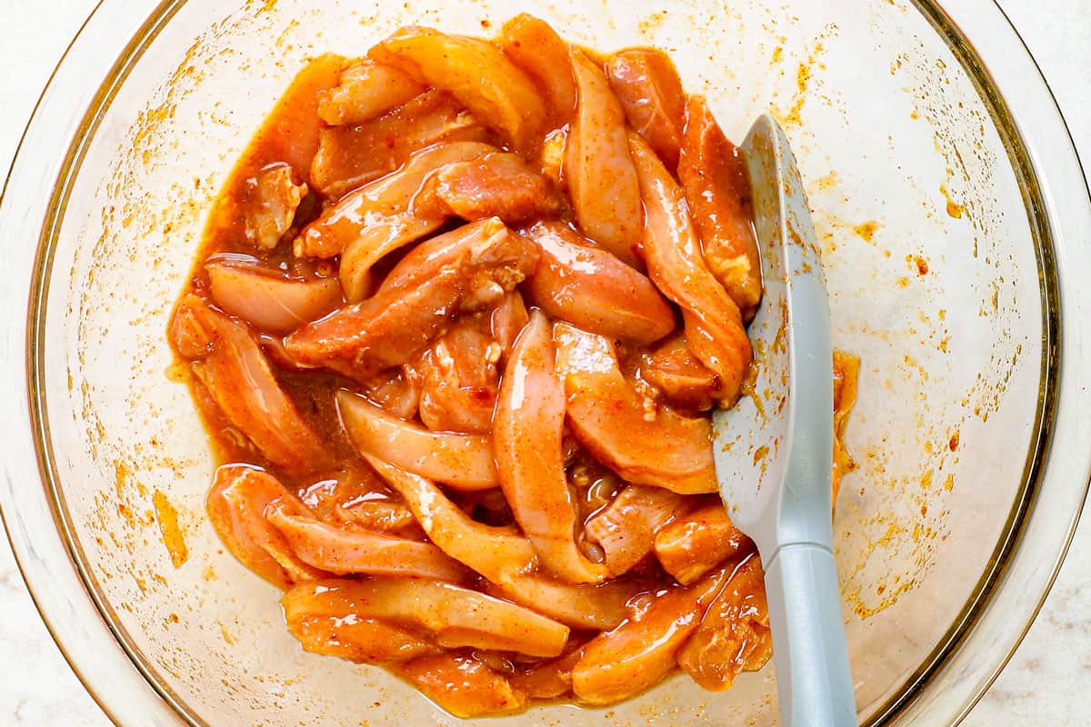 showing how to make spicy Dragon Chicken by adding chicken strips to whisked eggs, soy sauce and spices to marinate