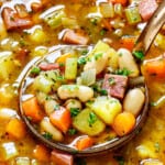 up close of a ladle of bean and ham soup showing the ham, white beans, carrots, celery and potatoes in a savory broth