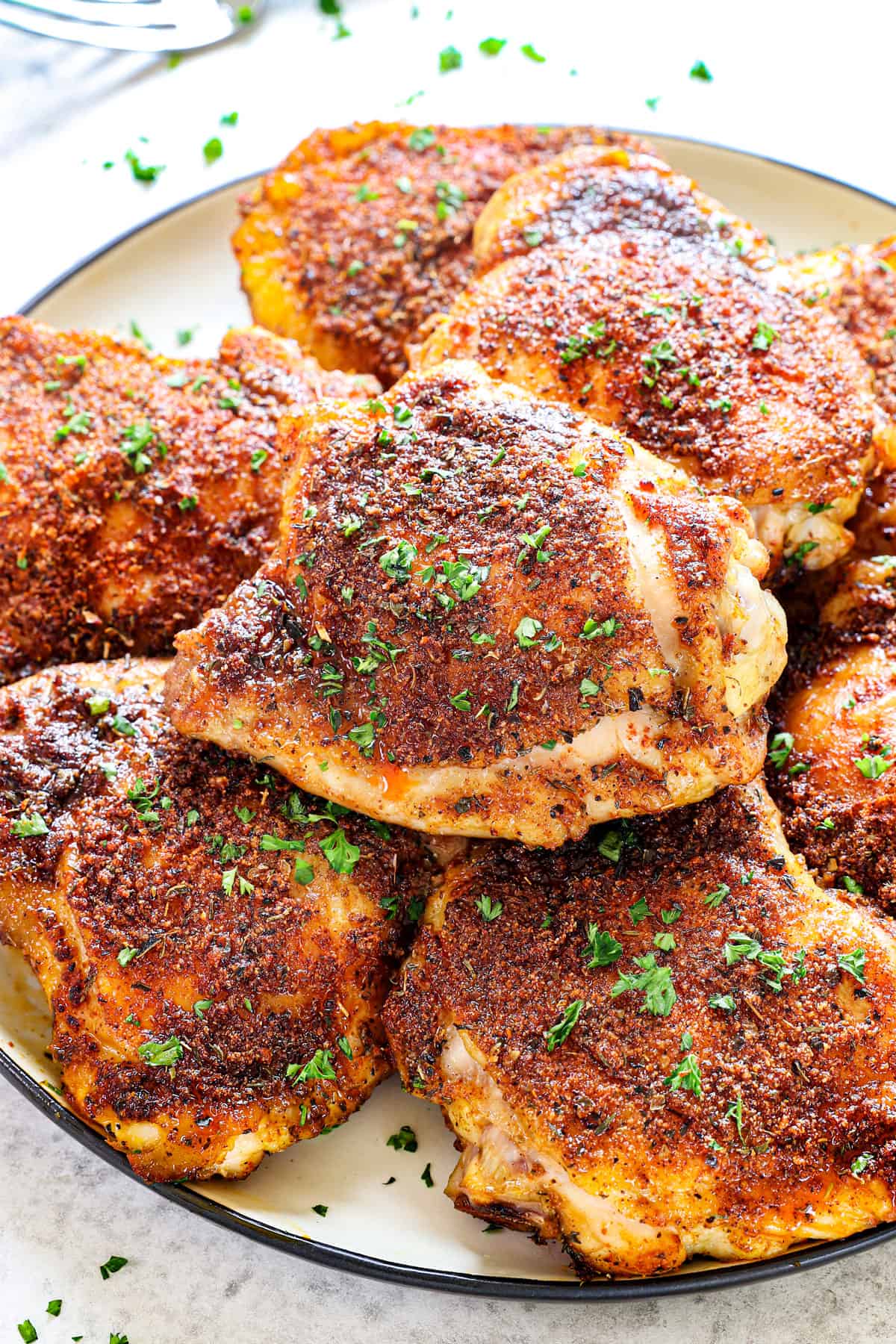 showing how to serve oven chicken thighs by adding to a plate and garnishing with parsley