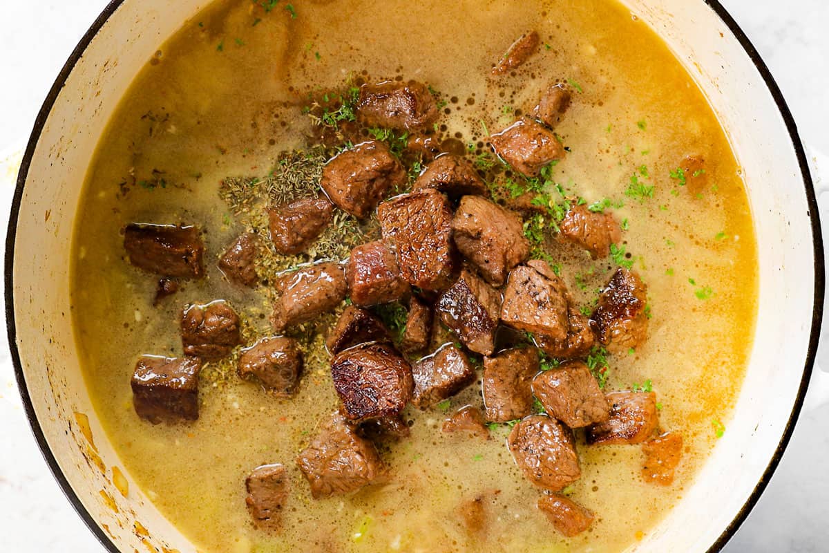 showing how to make Beef Noodle Soup by adding beef, broth and seasonings to the onions, carrots and celery
