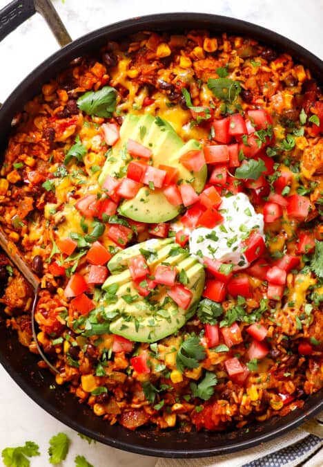 showing how to make chicken fiesta recipe by topping the skillet with sour cream, avocados and pico de gallo
