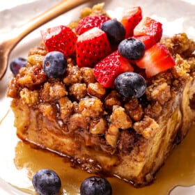 showing how to serve French Toast Casserole with a slice on a plate topped with strawberries and blueberries