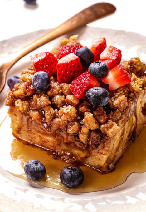 showing how to serve French Toast Casserole with a slice on a plate topped with strawberries and blueberries