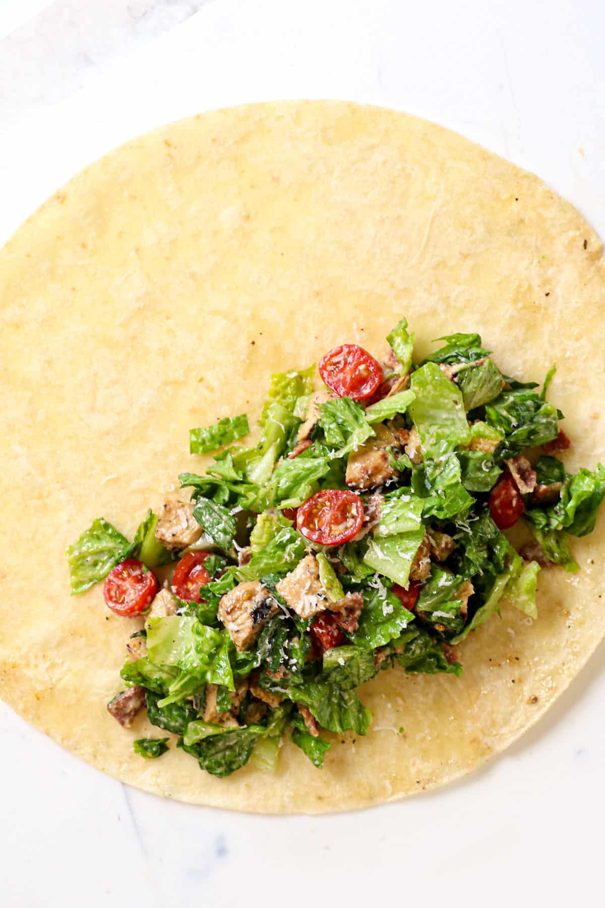 showing how to fold chicken Caesar wrap by adding filling to a tortilla