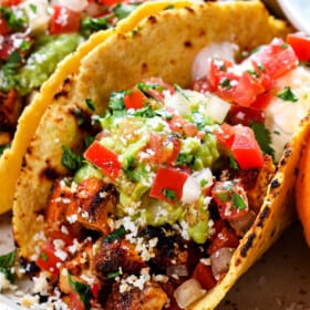 up close of chicken street tacos showing what they're made of: corn tortilla, chopped chicken, guacamole, pico de gallo and cotija cheese